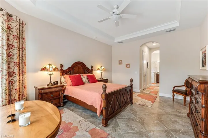 Bedroom with a tray ceiling, visible vents, arched walkways, stone finish flooring, and crown molding