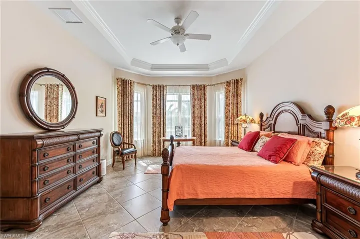 Tiled bedroom featuring a tray ceiling, visible vents, a ceiling fan, and ornamental molding