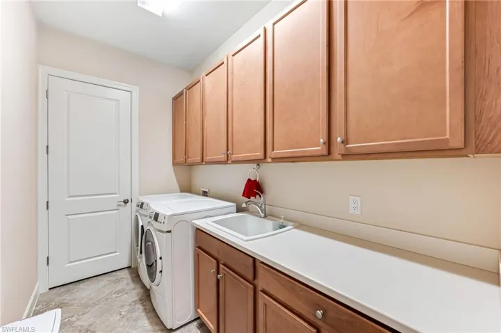 Clothes washing area with washing machine and dryer, baseboards, a sink, and cabinet space