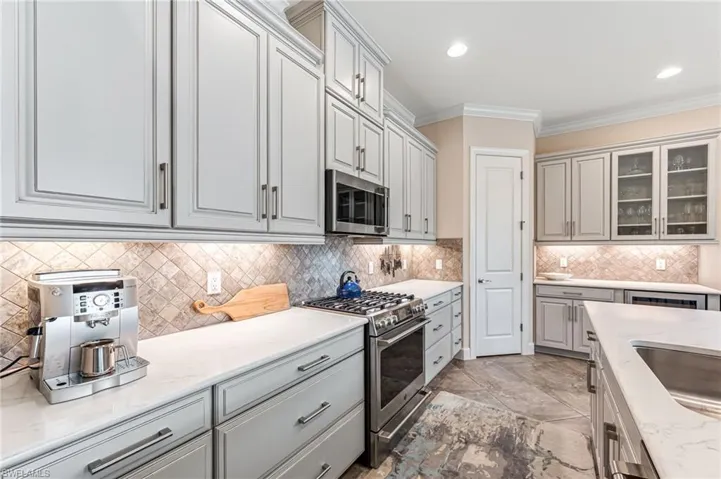 Kitchen with light stone counters, stainless steel appliances, ornamental molding, decorative backsplash, and glass insert cabinets