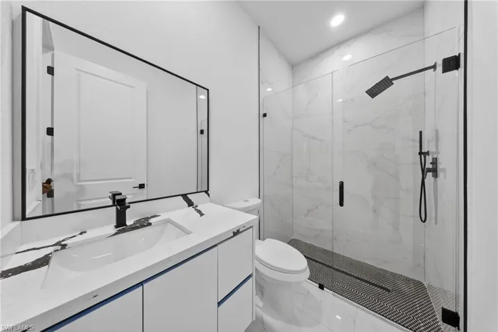 Modern bathroom featuring a frameless glass shower enclosure, a custom vanity with integrated sink, matte black fixtures, and large format wall and floor tiling