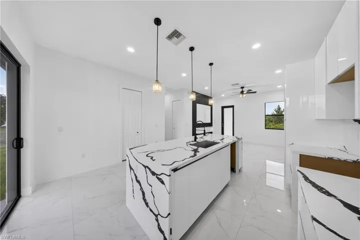 Gourmet kitchen featuring a waterfall island with a black and white veined countertop, integrated sink, and pendant lighting
