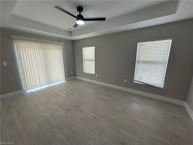 Spare room with a tray ceiling, a ceiling fan, plenty of natural light, and wood finish floors