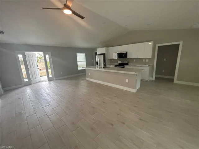 Kitchen with open floor plan, white cabinetry, a ceiling fan, an island with sink, and light countertops