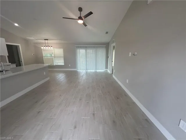 Unfurnished living room featuring lofted ceiling, wood finish floors, a ceiling fan, and a chandelier