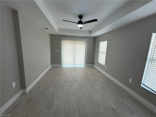 Unfurnished room with light wood finished floors, a ceiling fan, and a raised ceiling