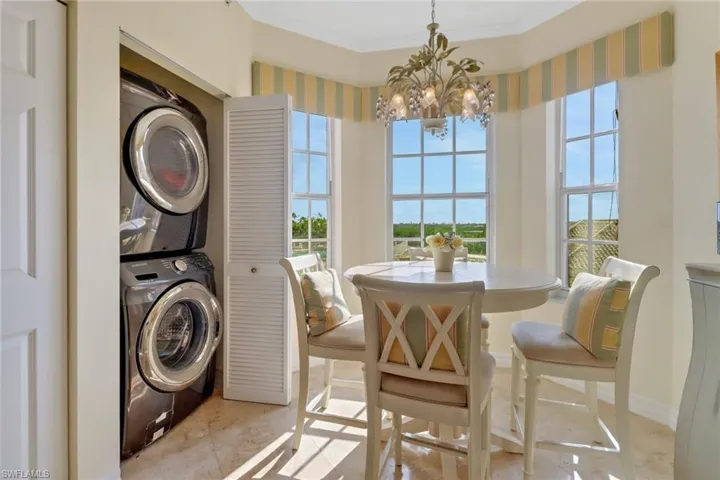 Clothes washing area featuring an inviting chandelier, stacked washer and dryer, light tile patterned flooring, and ornamental molding