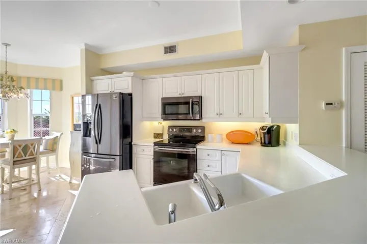 Kitchen featuring a notable chandelier, white cabinetry, stainless steel appliances, light tile patterned floors, and decorative light fixtures