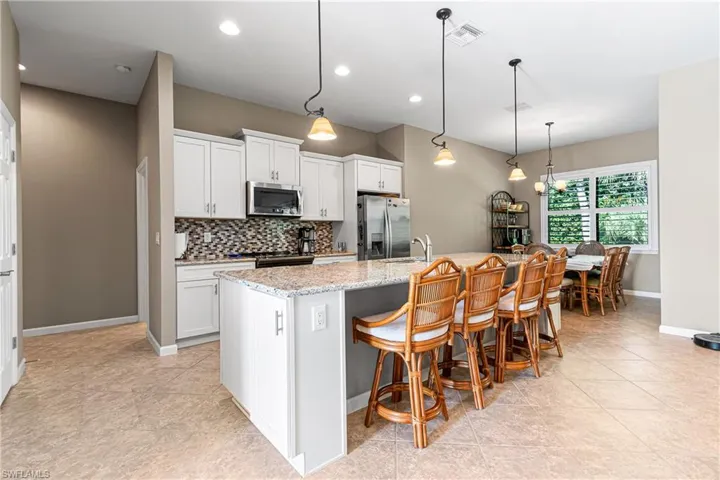 Kitchen featuring stainless steel appliances, backsplash, a breakfast bar area, a center island with sink, and white cabinetry