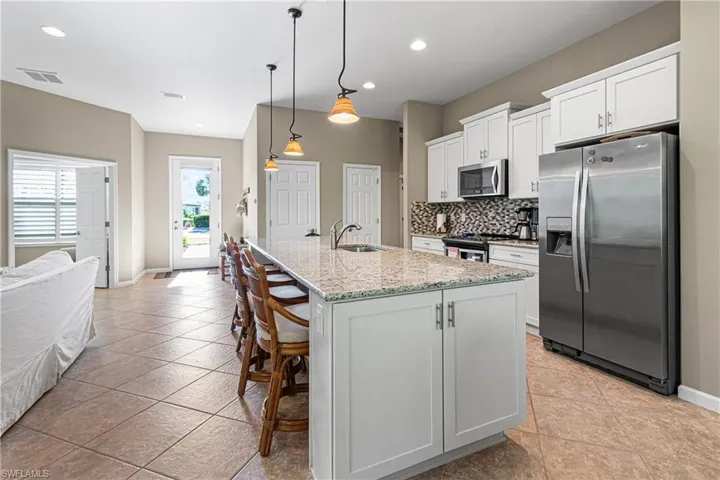 Kitchen featuring stainless steel appliances, decorative backsplash, a kitchen breakfast bar, white cabinetry, and an island with sink