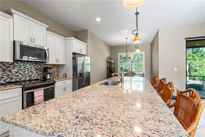 Kitchen with stainless steel appliances, a kitchen island with sink, tasteful backsplash, white cabinets, and plenty of natural light
