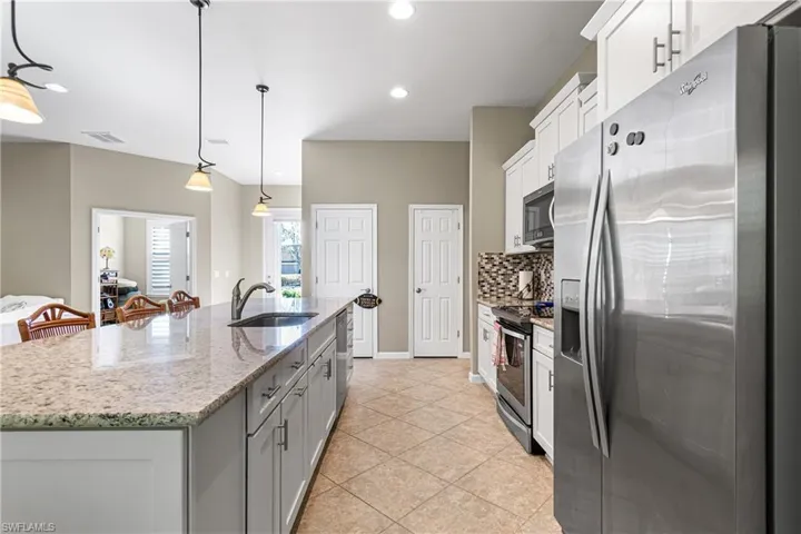 Kitchen featuring stainless steel appliances, decorative backsplash, a center island with sink, light stone countertops, and pendant lighting