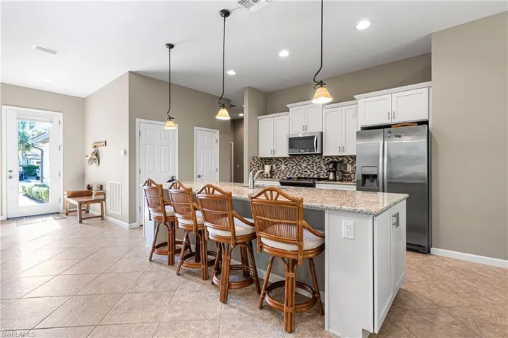 Kitchen featuring stainless steel appliances, backsplash, a center island with sink, white cabinetry, and a breakfast bar
