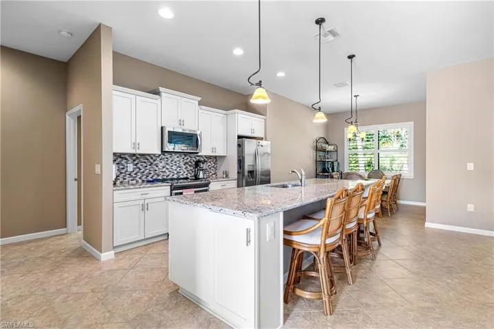 Kitchen featuring appliances with stainless steel finishes, a center island with sink, tasteful backsplash, white cabinets, and recessed lighting