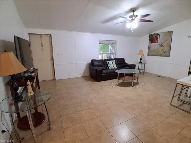Living room with lofted ceiling, ceiling fan, and light tile patterned floors