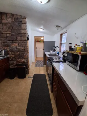 Kitchen featuring stove, dark wood finish cabinetry, black microwave, light countertops, and separate washer and dryer