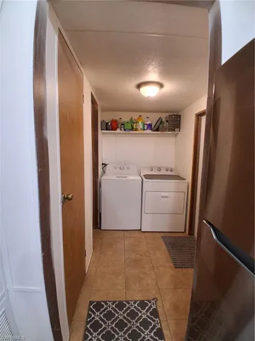 Laundry room with washing machine and clothes dryer, a textured ceiling, and light tile patterned floors