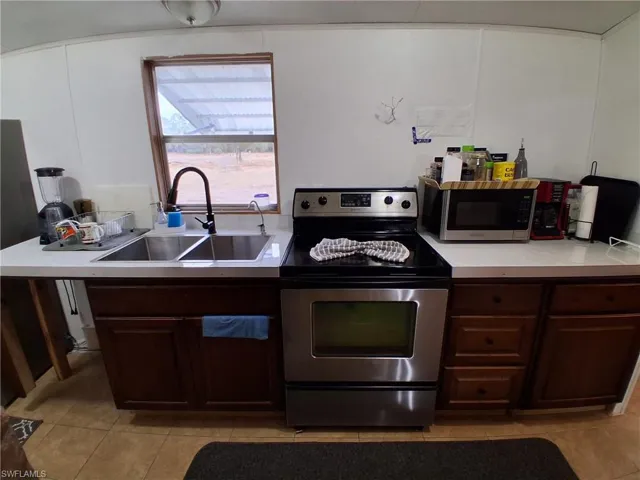 Kitchen with electric range, dark wood finish cabinets, light tile patterned floors, and light countertops