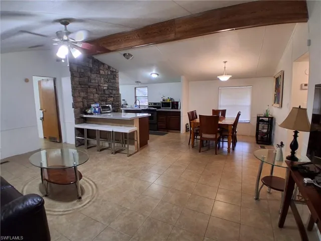 Living room featuring vaulted ceiling with beams, a ceiling fan, and light tile patterned flooring