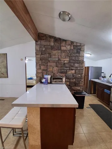 Kitchen with light countertops, fridge, lofted ceiling with beams, light tile patterned flooring, and a breakfast bar area