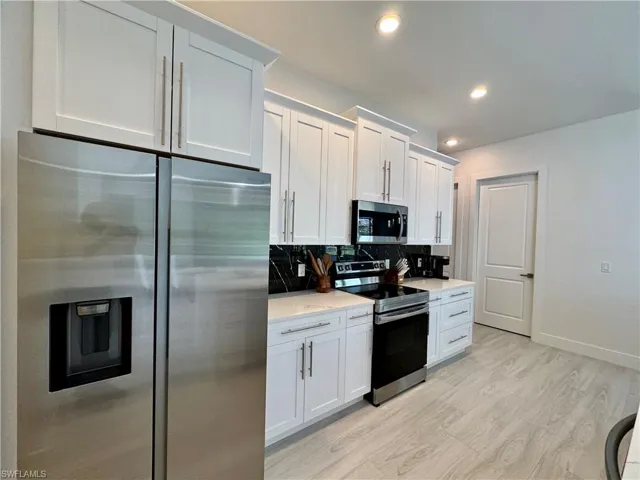 Kitchen featuring decorative backsplash, stainless steel appliances, and white cabinetry