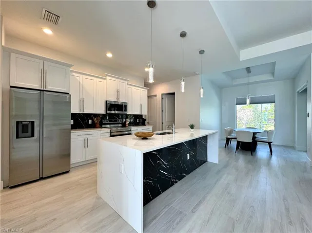 Kitchen featuring white cabinetry, hanging light fixtures, stainless steel appliances, tasteful backsplash, and a kitchen island with sink