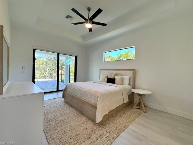 Bedroom featuring ceiling fan, light wood-type flooring, access to outside, and a tray ceiling