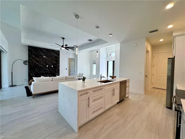 Kitchen with white cabinets, sink, hanging light fixtures, an island with sink, and appliances with stainless steel finishes