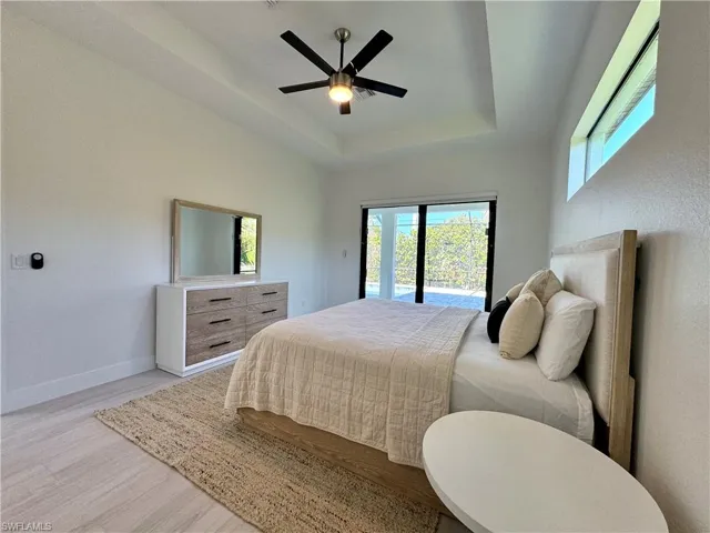 Bedroom with a raised ceiling, access to exterior, ceiling fan, and light wood-type flooring