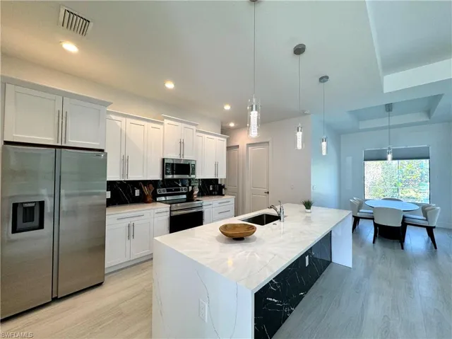 Kitchen with pendant lighting, backsplash, an island with sink, white cabinetry, and stainless steel appliances