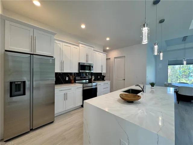 Kitchen with appliances with stainless steel finishes, white cabinetry, pendant lighting, and sink