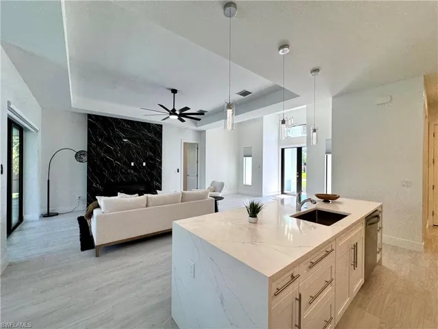 Kitchen with light stone countertops, dishwasher, sink, decorative light fixtures, and a center island with sink