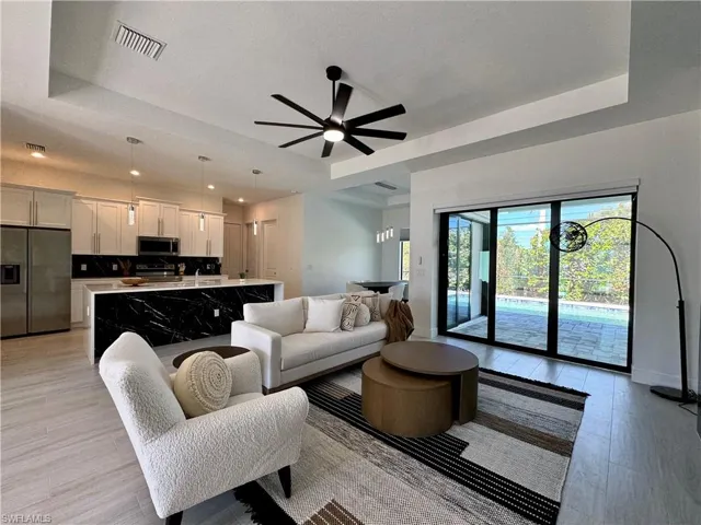 Living room featuring a raised ceiling, ceiling fan, and light hardwood / wood-style flooring