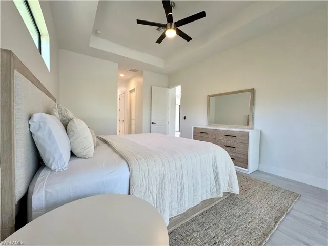 Bedroom with a raised ceiling, ceiling fan, and light hardwood / wood-style flooring