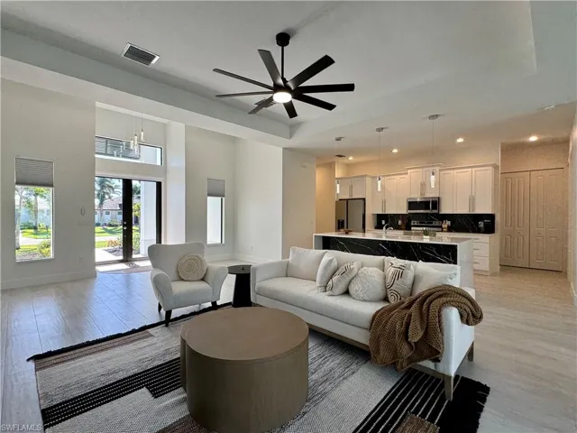 Living room with ceiling fan with notable chandelier, a raised ceiling, french doors, and light hardwood / wood-style flooring