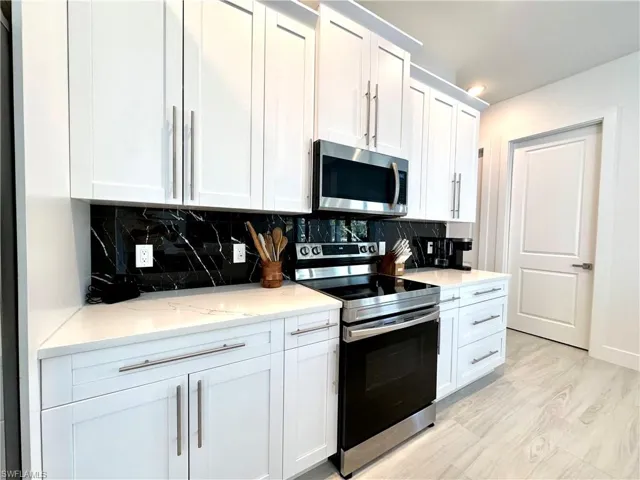 Kitchen featuring backsplash, white cabinetry, light stone countertops, and appliances with stainless steel finishes