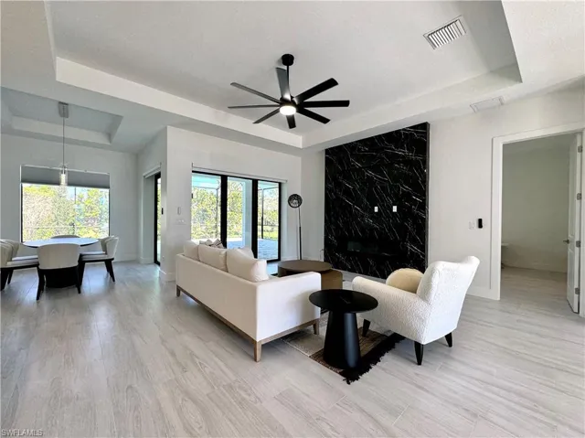 Living room with ceiling fan, light hardwood / wood-style flooring, and a tray ceiling
