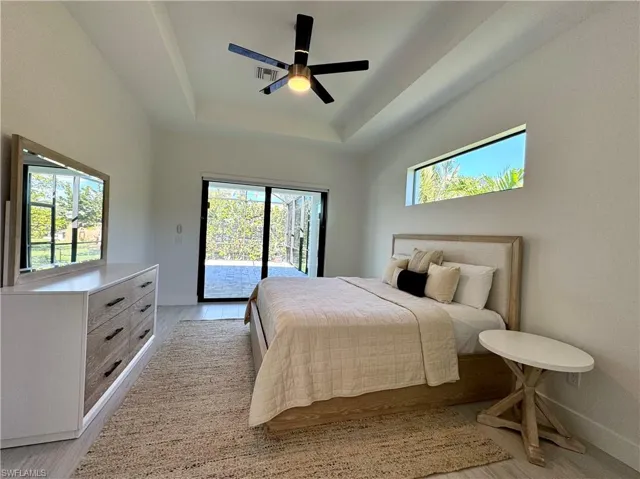Bedroom featuring access to outside, multiple windows, a tray ceiling, and ceiling fan