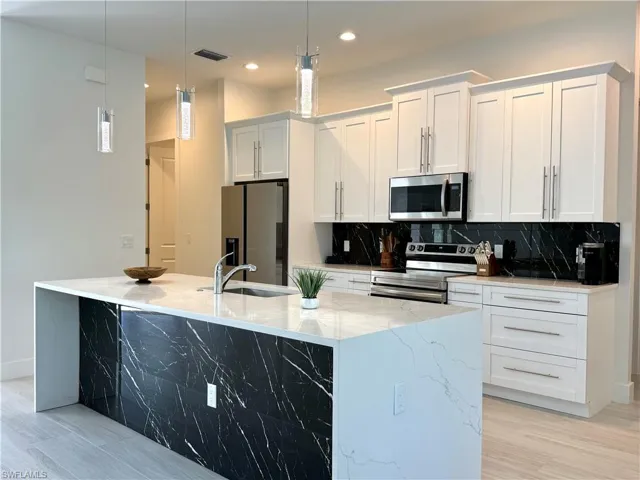 Kitchen featuring stainless steel appliances, tasteful backsplash, pendant lighting, a center island with sink, and white cabinets
