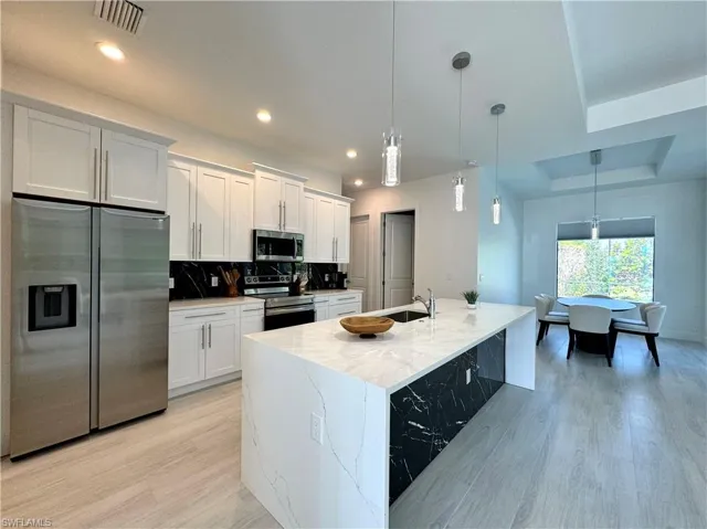 Kitchen featuring white cabinets, appliances with stainless steel finishes, and decorative light fixtures