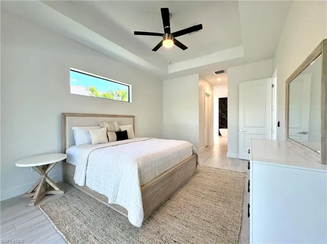 Bedroom with a tray ceiling, ceiling fan, and light hardwood / wood-style floors