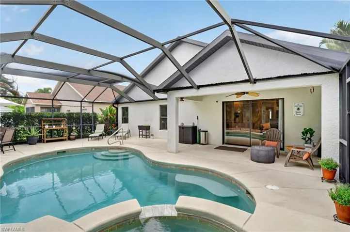 Screened pool enclosure featuring a freeform swimming pool with integrated steps, a spacious concrete deck, and a covered patio area with a ceiling fan