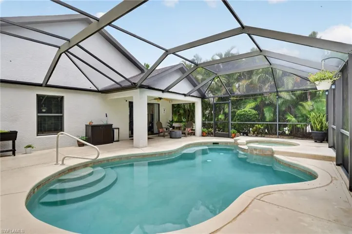 Screened-in pool area featuring a freeform swimming pool with integrated steps, an elevated spa, and a surrounding concrete deck