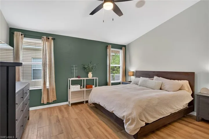 Vaulted ceiling bedroom featuring wood-finish flooring, a ceiling fan, and two windows with blinds