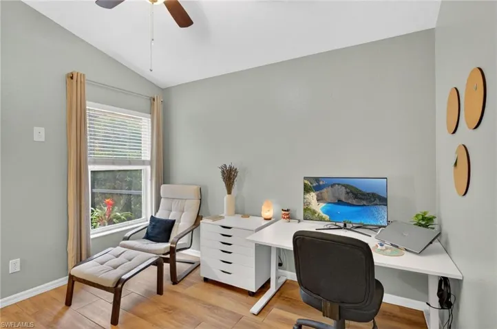 Vaulted ceiling room featuring wood-finish flooring, a window with blinds, and light-colored walls