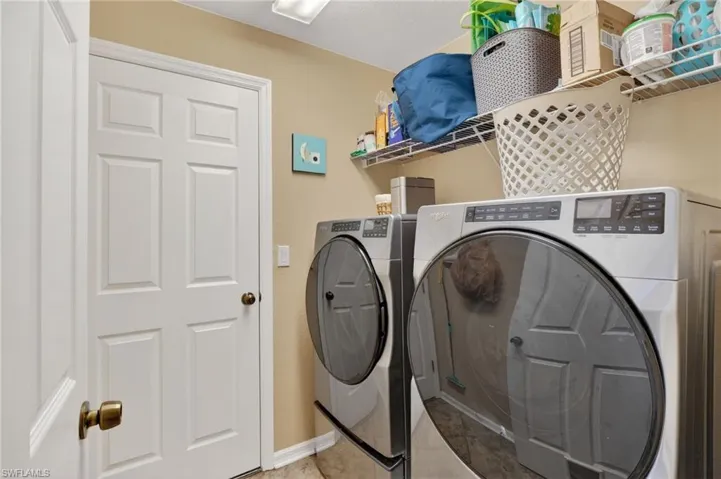 Dedicated utility space featuring a neutral wall color, white six-panel door, square ceiling light fixture, and tile flooring