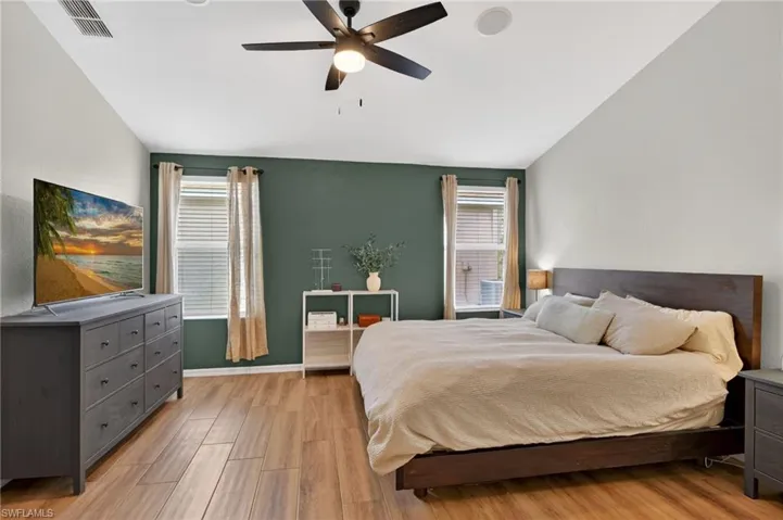 Interior room featuring wood-finish flooring, a ceiling fan with integrated lighting, and multiple windows with blinds