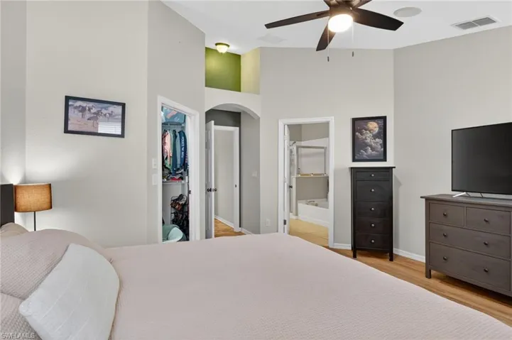 Vaulted ceiling room featuring a ceiling fan, wood-finish flooring, and an open closet with built-in shelving