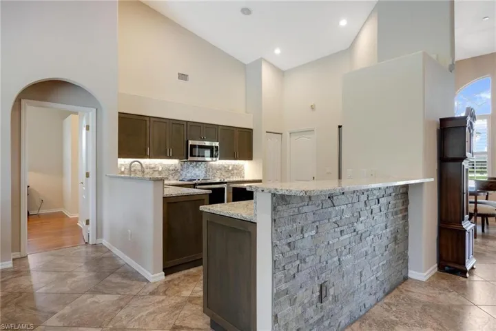Kitchen featuring a center island, stainless steel appliances, light stone counters, tasteful backsplash, and light tile flooring