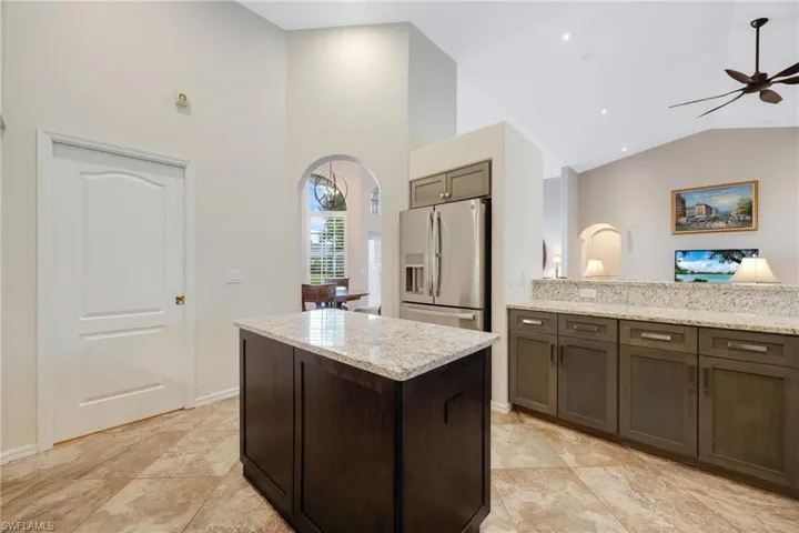 Kitchen with light tile floors, stainless steel fridge with ice dispenser, ceiling fan, and vaulted ceiling